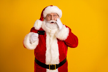Santa in red costume with white fur trim holds a card and surprises you in a bright yellow studio as he spreads holiday joy and playful cheer