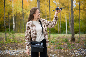 A young woman stands in a vibrant forest filled with colorful autumn leaves. She holds a drone, ready to explore the skies and capture stunning views.