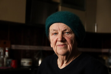 portrait of a senior woman, approximately 75 years old, captured indoors. Her expressive blue eyes convey a deep sense of sadness. 75 year old woman portrait wearing beret
