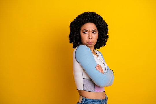 Young woman in casual attire against yellow backdrop displaying crossed arms and a thoughtful expression