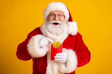 Santa in red suit with white fur holding fries in a red container smiles against a bright yellow backdrop perfect for christmas and holiday themes