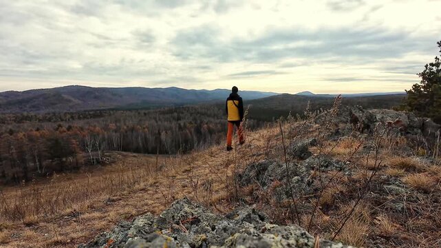 Hiking enthusiast in bright clothing views expansive valley scene with thoughtfulness, An adventurous man in yellow coat gazes across layered hills into horizon with reflective calmness