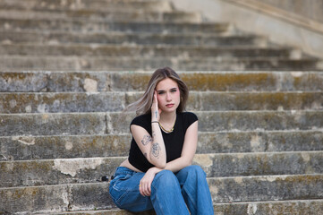 Young, pretty, tattooed blonde woman, wearing jeans, black shirt and sunglasses, sitting on the...
