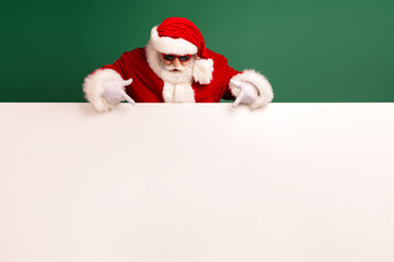 Santa in red costume points to a large blank sign against a green background for Christmas promotions