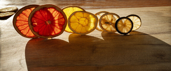 Various dried citrus fruits backlit on wood with shadows. Visible fruit texture with natural patterns for christmas decorations.