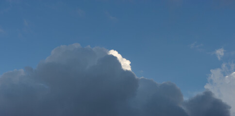 A dark rain cloud covers a white cloud against a blue sky.