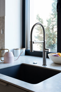 Modern kitchen sink with silver faucet near window and granite countertop. Interior of kitchen with detail.	Close up. Vertical.