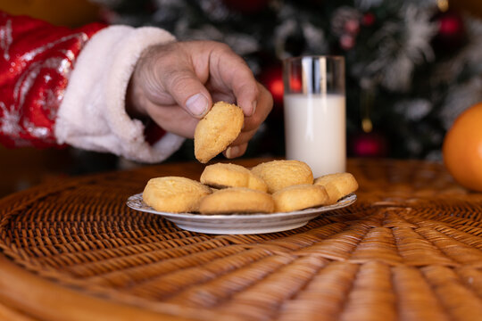 Santa takes a cookie from a plate left out with a glass of milk