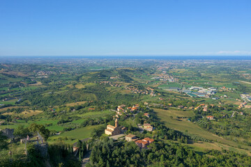 Aerial panoramic view of rolling hills, a village, and the Adriatic Sea coastline near Rimini, Italy.
