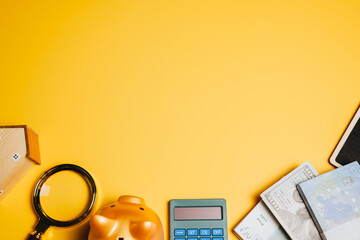Financial planning background. Piggy bank, calculator, house model, and cash on yellow surface,...