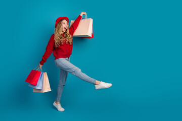 Cheerful young woman in a stylish red sweater joyfully holding colorful shopping bags against a...