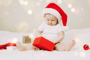 Baby wearing a Santa hat curiously examines a red gift box, surrounded by festive decorations. The scene captures the magic and wonder of a baby's Christmas experience.
