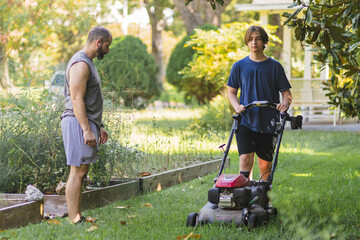 Man stands and watches as son mows the lawn