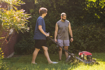 Father looks at lawnmower while son pushes it