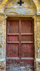 Old weathered door: Rustic red wooden door within the embrace of a aged stone wall with archway. Capture a sense of historical elegance and enduring beauty