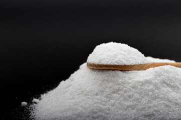 Iodated salt pile is poured out in front of black background with wooden spoon. Textured horizontal photo, closeup. V41.