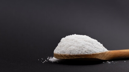 Iodated salt scoop in front of black background with wooden spoon. Textured horizontal photo, closeup. V39.