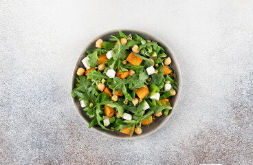 Healthy arugula salad with roasted pumpkin, chickpeas, feta cheese, pistachios on gray background. Top view. 