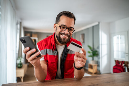 Man smiling while holding credit card and smartphone shopping online - Powered by Adobe
