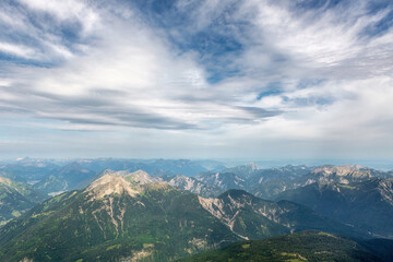Summer mountain view from Zugspitze peak overlooking alpine valleys, rocky cliffs and green slopes under a bright blue sky