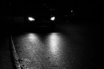 Black car with headlights driving on wet asphalt in the night.