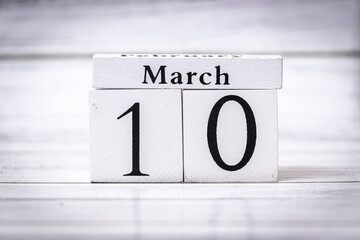 March 10 displayed on vintage wooden calendar blocks against a light wooden background, symbolizing the arrival of spring and daily life organization. Unique date presentation.