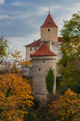 Fototapeta premium Historical stone castle tower Daliborka and behind it the Black Tower of Prague Castle, with a red tiled roof stands surrounded by the autumn-colored leaves of the trees. Prague, Czech Republic 