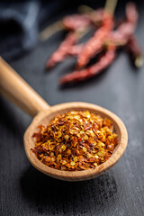 Red chili peppers flakes. Milled spicy peppers on wooden scoop on black table.