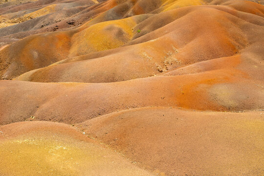 Close view of Chamarel Seven Coloured Earth rippled dunes with warm tones, soft curves, and fine granular texture