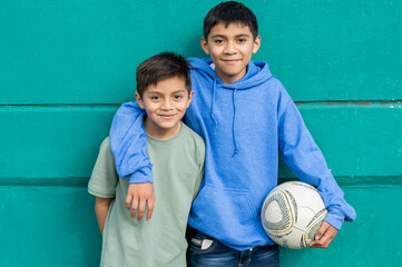 Two smiling hispanic brothers hugging holding soccer ball