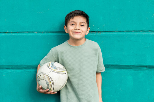 Young boy smiling, holding soccer ball against teal wall