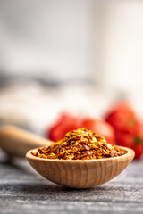 Red chili peppers flakes. Milled spicy peppers on wooden scoop on kitchen table.