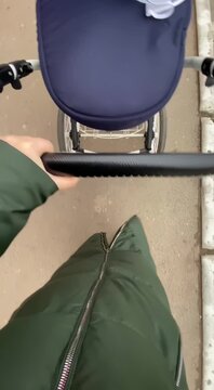 Person pushes a baby stroller on a sidewalk. Overhead view of a parent walking with a pram.