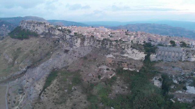 Aerial view: ancient village of Gerace Calabria Italy built on rocky mountain top at sunrise with dramatic cliffs and historic stone houses symbolizing heritage and Mediterranean culture