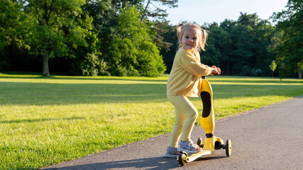 Child with scooter. Yellow riding toddler fun. Summer activity outdoor road.