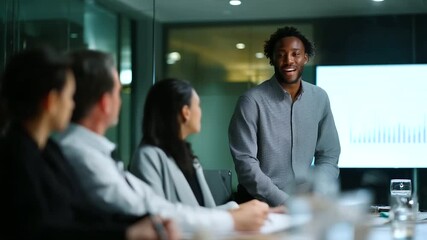 Business meeting in a modern glass-walled conference room, diverse team of professionals sitting around a table while a presenter stands and points at a large digital screen showin - Powered by Adobe