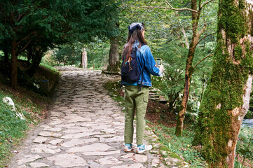 A girl in a park photographs nature with her smartphone, blending modern technology with natural surroundings.