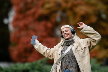 Young woman enjoying music, dancing with headphones outdoors