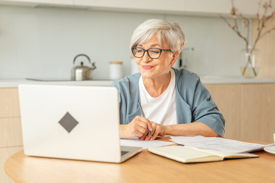 Online education courses webinar concept. Middle aged senior woman using laptop computer writing notes. Focused mature old woman enjoying studying online from home written records doing online work