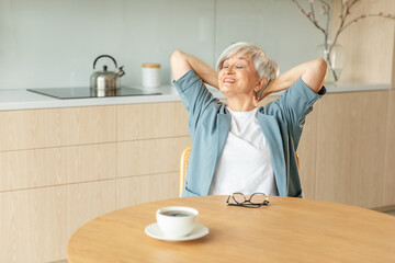 Senior old woman feeling relaxed stretching arms in kitchen at home. Smiling mature woman stretching hands feel positive optimistic fresh on bright morning new day. Good mood happy elderly lifestyle