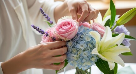 Womans hands carefully arranging a colorful bouquet of pink roses, blue hydrangea, and white lily.