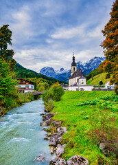 Naklejka premium vertical: St. Sebastian Church and riverside alpine houses in autumn, Ramsau, Germany St. Sebastian Church and village framed by autumn trees, Ramsau bei Berchtesgaden, Germany