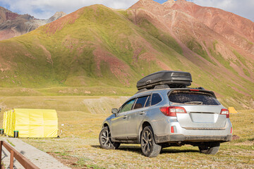 Obraz premium A trip in a prepared all-terrain vehicle, with a roof box, into the high mountains across impassable and dirt roads against the backdrop of snow-capped peaks and sunshine