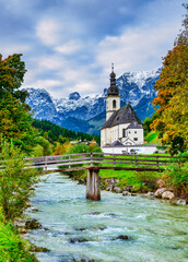 Fototapeta premium Vertical shot: St. Sebastian Church, river, and autumn trees, Ramsau bei Berchtesgaden, Germany