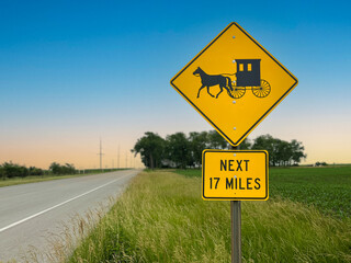 Yellow caution sign on the side of the road cautions drivers to be on the lookout for slower moving horse and buggy traffic. Located in Amish Country near Arthur, Illinois, USA. Selective focus.