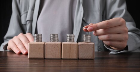 Woman stacking coins and cubes at wooden table, closeup