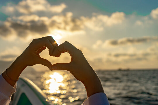 Hands heart sunset, creating a romantic shape against a beautiful golden ocean horizon.