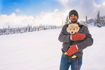 Smiling man standing in a snowy winter landscape keeping a golden retriever puppy warm under his coat, USA