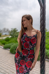 Naklejka premium Woman floral dress park. Beautiful young woman in summer dress leaning against column looking away