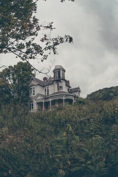 Abandoned Victorian-style house with decaying architecture and overgrown surroundings